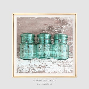 May include: Three vintage blue glass jars with wire handles, arranged in a row on a weathered wood background.