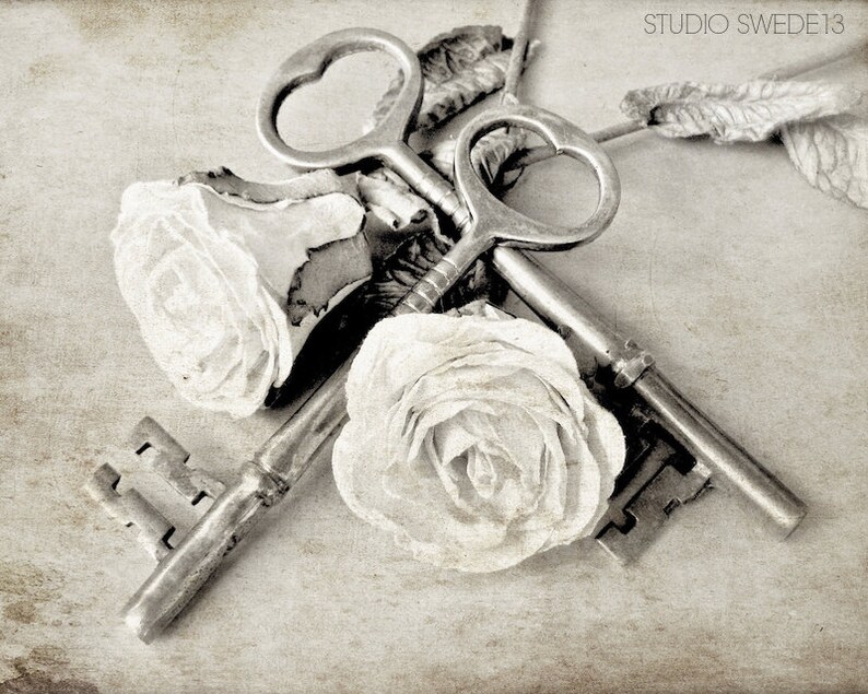 May include: Two antique keys with ornate designs are intertwined with two white fabric roses. The keys are silver and have a vintage look. The roses are delicate and soft, adding a romantic touch to the image.