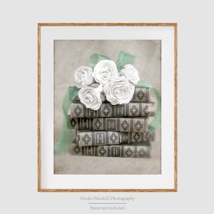 May include: A framed print featuring a stack of antique books adorned with white roses and a green ribbon. The books have ornate, patterned covers. The print is in a wooden frame, with the text "Studio Swedel3 Photography" at the bottom.