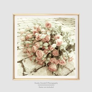 May include: A bouquet of pink roses with green stems and leaves, arranged on a brick pathway. The roses are faded and have a vintage aesthetic.