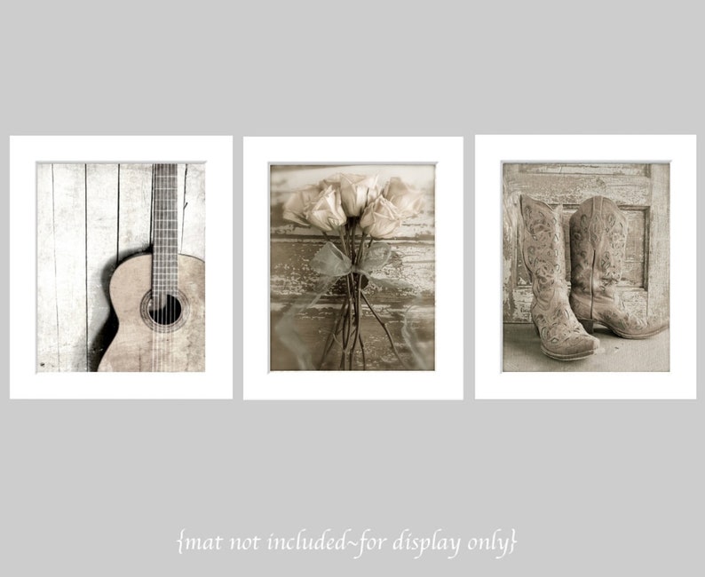 Op de afbeelding: Een set van drie sepia-getinte prints met een rustieke houten achtergrond. De eerste print toont een houten akoestische gitaar, de tweede print toont een boeket rozen en de derde print toont een paar bruine cowboylaarzen.