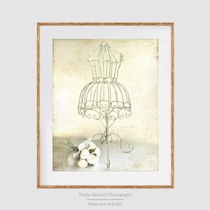 May include: A vintage-style metal dress form with a white background. The dress form is green and has a delicate design. A bouquet of white flowers is in the foreground.