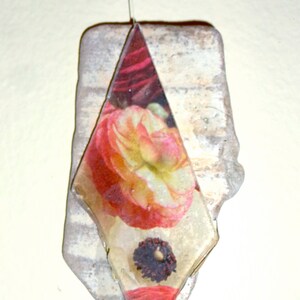 May include: A diamond-shaped piece of glass with a pressed flower design. The flower is red, yellow, and white with a dark brown center. The glass is mounted on a piece of rough, white, textured stone.