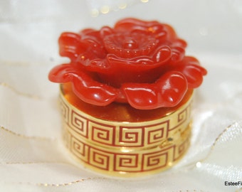 May include: A small red rose-shaped trinket box with a gold lid decorated with a repeating geometric pattern.