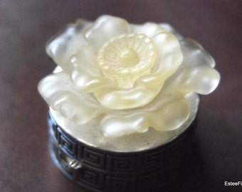May include: A white porcelain trinket box with a floral design. The lid is shaped like a flower with a raised center and ruffled edges.
