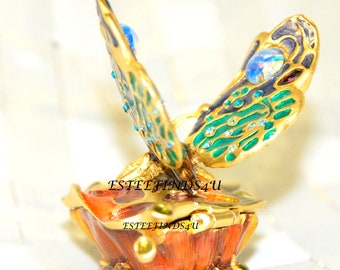 May include: A gold-tone trinket box with a butterfly design. The butterfly has green, blue, and black wings with iridescent accents. The box is open and has a red and orange interior.