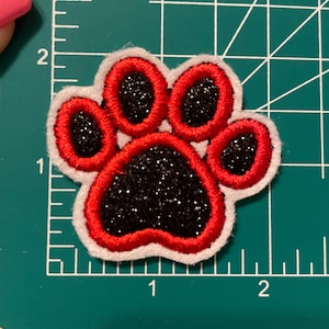 May include: Red and black paw print iron-on patch with white edging. The paw print is filled with black glitter.
