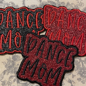 May include: Three iron-on patches with the text "Dance Mom" in black and red glitter. The patches are in different styles and sizes.