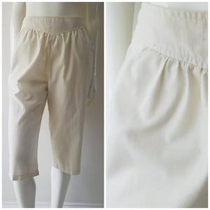 May include: A pair of off-white capri pants with a wide waistband and a slightly gathered front.