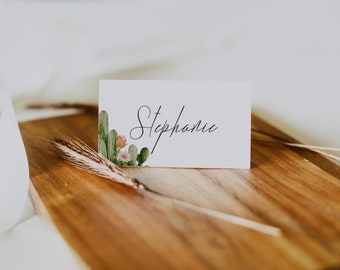 May include: White place card with a cactus and flower design on the left side. The name "Stephanie" is written in black cursive on the right side of the card.