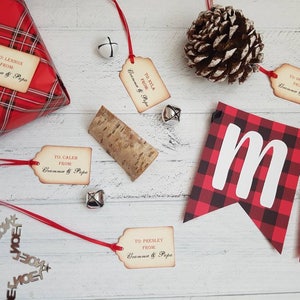Puede incluir: Papel de regalo a cuadros rojos y negros con una etiqueta de regalo que dice "TO: LENNOX FROM: Gramme & Papa". Hay varias otras etiquetas de regalo con un texto similar, una pi&ntilde;a y una pancarta que dice "Merry".
