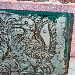 May include: A carved wooden panel with a green border, featuring a detailed design of two birds with intricate feathers and a faded silver paint finish.