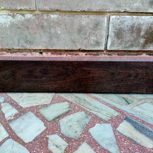 May include: A dark brown wooden plank with a smooth surface. The plank is lying on a tiled floor.