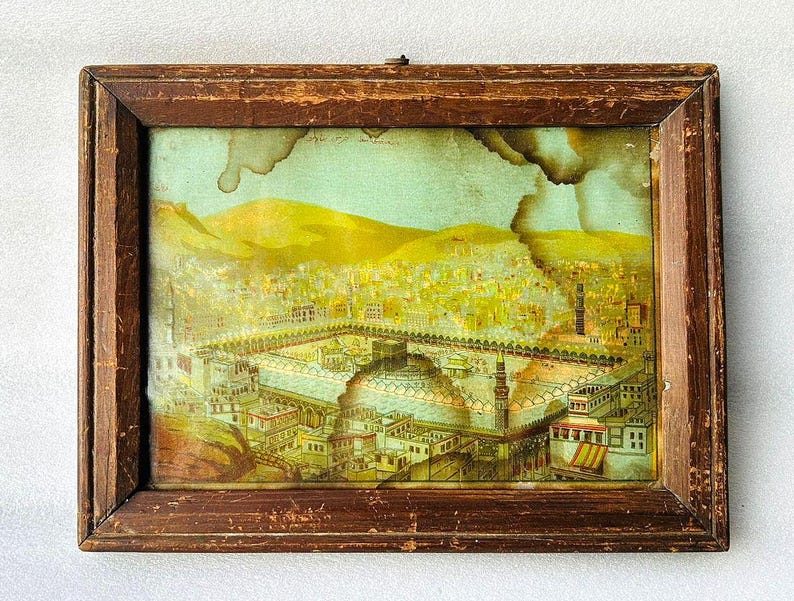 Puede incluir: Una impresi&oacute;n enmarcada vintage que representa una ilustraci&oacute;n detallada de una ciudad con una mezquita en el centro. La impresi&oacute;n est&aacute; en un marco de madera con un acabado marr&oacute;n. La ilustraci&oacute;n est&aacute; en tonos de amarillo, marr&oacute;n y verde.