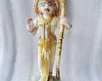 May include: White marble statue of a Hindu deity with a golden crown, holding a staff. The statue is standing on a white marble base.