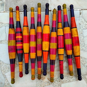 May include: A set of 13 wooden exercise clubs with alternating bands of red, yellow, black, and green paint.