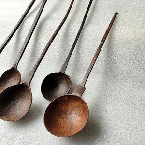 以下が含まれることがあります： 長い柄のついたアンティークな鉄製のレードルが5つ。レードルはさび付いており、濃い茶色をしています。