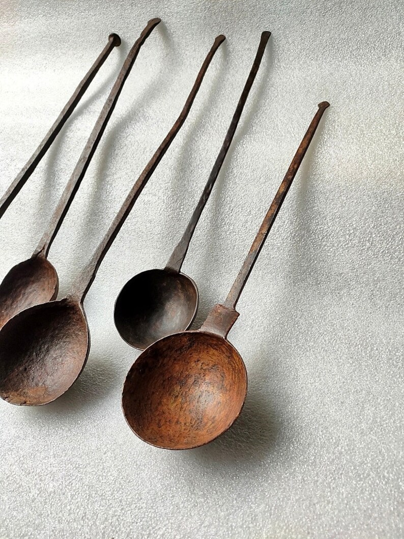 以下が含まれることがあります： 長い柄のついたアンティークな鉄製のレードルが5つ。レードルはさび付いており、濃い茶色をしています。