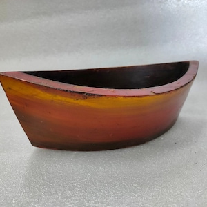 Peut inclure: Un plat en bois en forme de bateau avec une finition peinte en dégradé rouge, orange et jaune. Le plat est incurvé et a un fond arrondi.