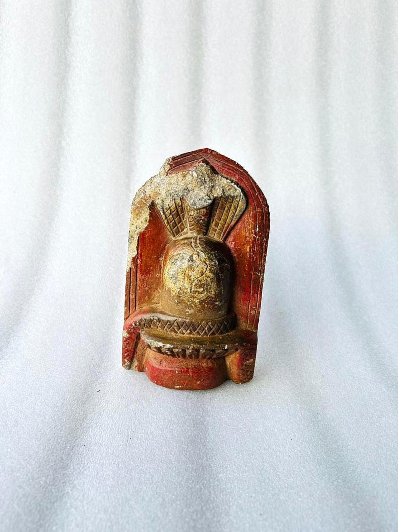 Puede incluir: Una peque&ntilde;a escultura de piedra roja y dorada de una deidad con una corona y detalles intrincados.