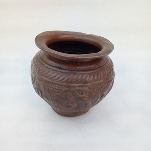 Puede incluir: Una pequeña olla redonda de cobre con intrincados tallados. La olla tiene una boca ancha y un fondo redondeado. Los tallados son de estilo floral.