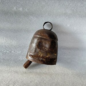 May include: A brown metal bell with a wooden handle and intricate carvings. The bell has a circular loop at the top for hanging.