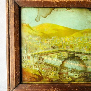 Puede incluir: Una ilustraci&oacute;n vintage enmarcada de la Kaaba en La Meca, Arabia Saudita. La imagen est&aacute; en un marco de madera con un acabado marr&oacute;n claro. La ilustraci&oacute;n est&aacute; en un esquema de color amarillo, verde y azul. El texto de la imagen dice "La Meca, Arabia Saudita".