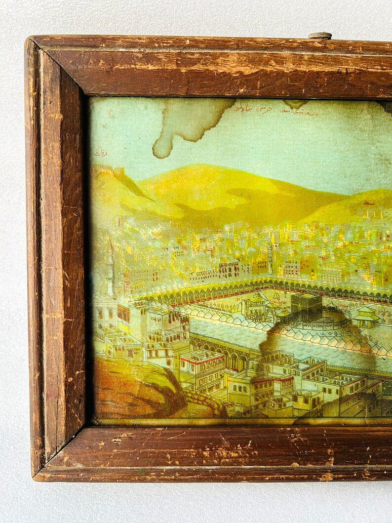 Puede incluir: Una ilustraci&oacute;n vintage enmarcada de la Kaaba en La Meca, Arabia Saudita. La imagen est&aacute; en un marco de madera con un acabado marr&oacute;n claro. La ilustraci&oacute;n est&aacute; en un esquema de color amarillo, verde y azul. El texto de la imagen dice "La Meca, Arabia Saudita".