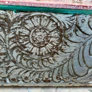 May include: Close-up of a weathered, gray wooden panel with intricate carvings of a floral design. The carvings feature a central circular motif surrounded by leaves and swirls.