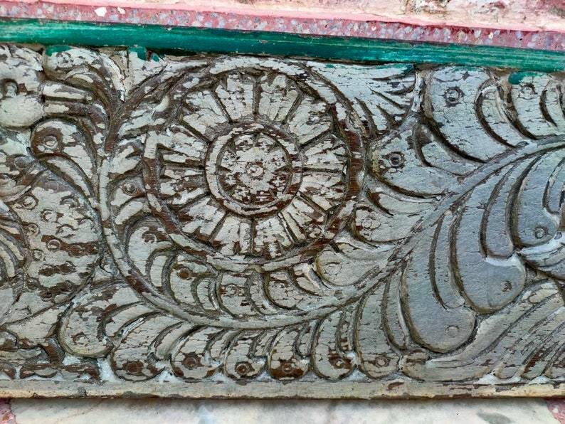 May include: Close-up of a weathered, gray wooden panel with intricate carvings of a floral design. The carvings feature a central circular motif surrounded by leaves and swirls.