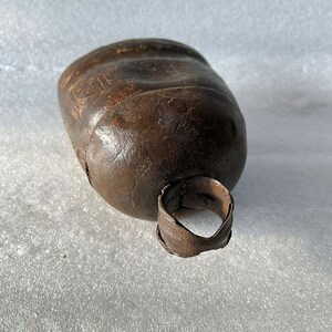 May include: A brown metal cowbell with a worn surface and a metal ring handle.