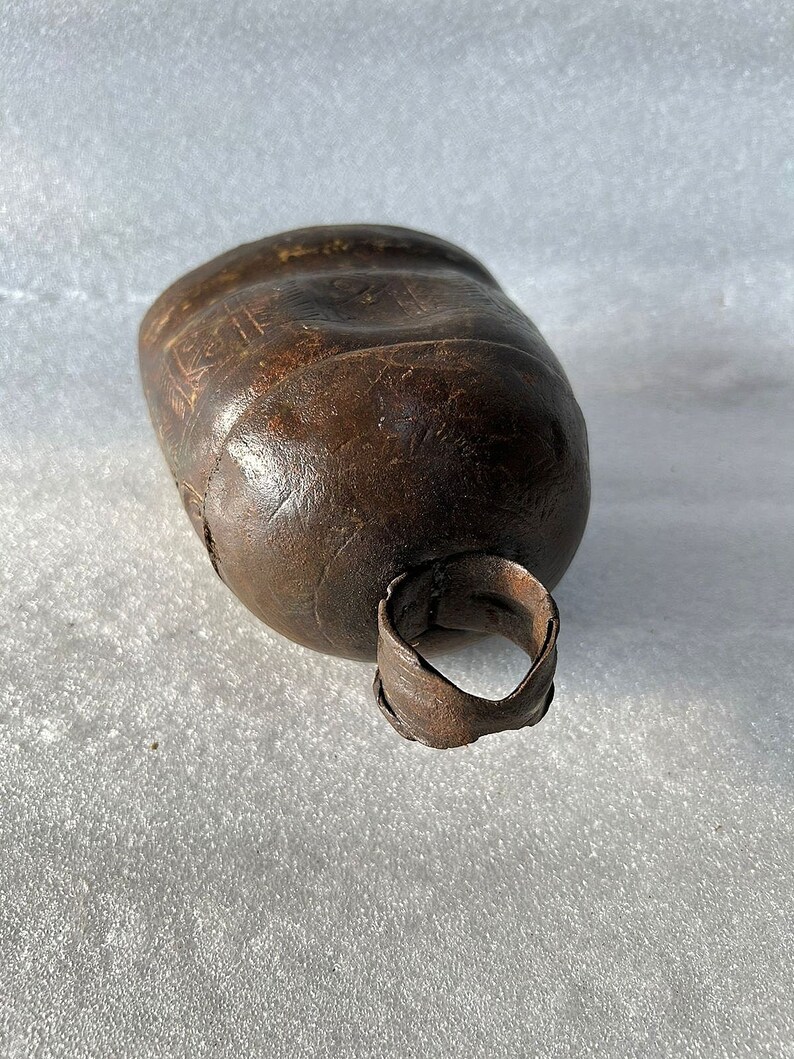 May include: A brown metal cowbell with a worn surface and a metal ring handle.