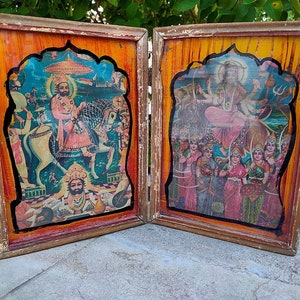 May include: Two framed religious prints. The prints feature colorful illustrations of deities and figures, set against a backdrop of orange and yellow. The frames are made of wood with a distressed finish, adding a vintage aesthetic.