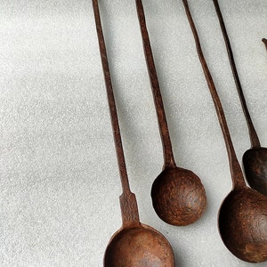 以下が含まれることがあります： 長い柄のついたアンティークの金属製のレードルが5つ。レードルはさびた茶色で、使い古された、古びた外観をしています。