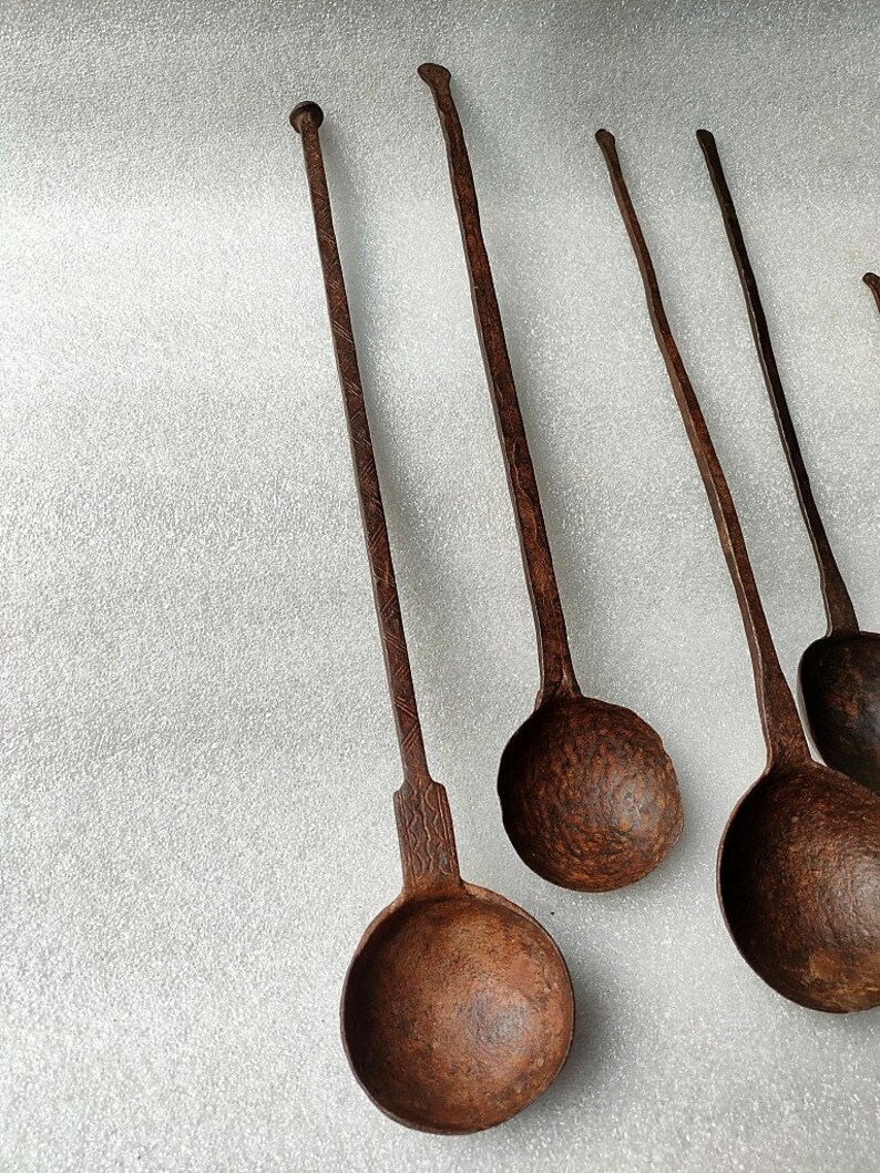 以下が含まれることがあります： 長い柄のついたアンティークの金属製のレードルが5つ。レードルはさびた茶色で、使い古された、古びた外観をしています。