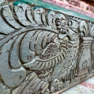 May include: Close-up of a weathered, gray wooden carving with intricate details of a mythical creature with a beak and feathers. The carving is painted with shades of green and white.