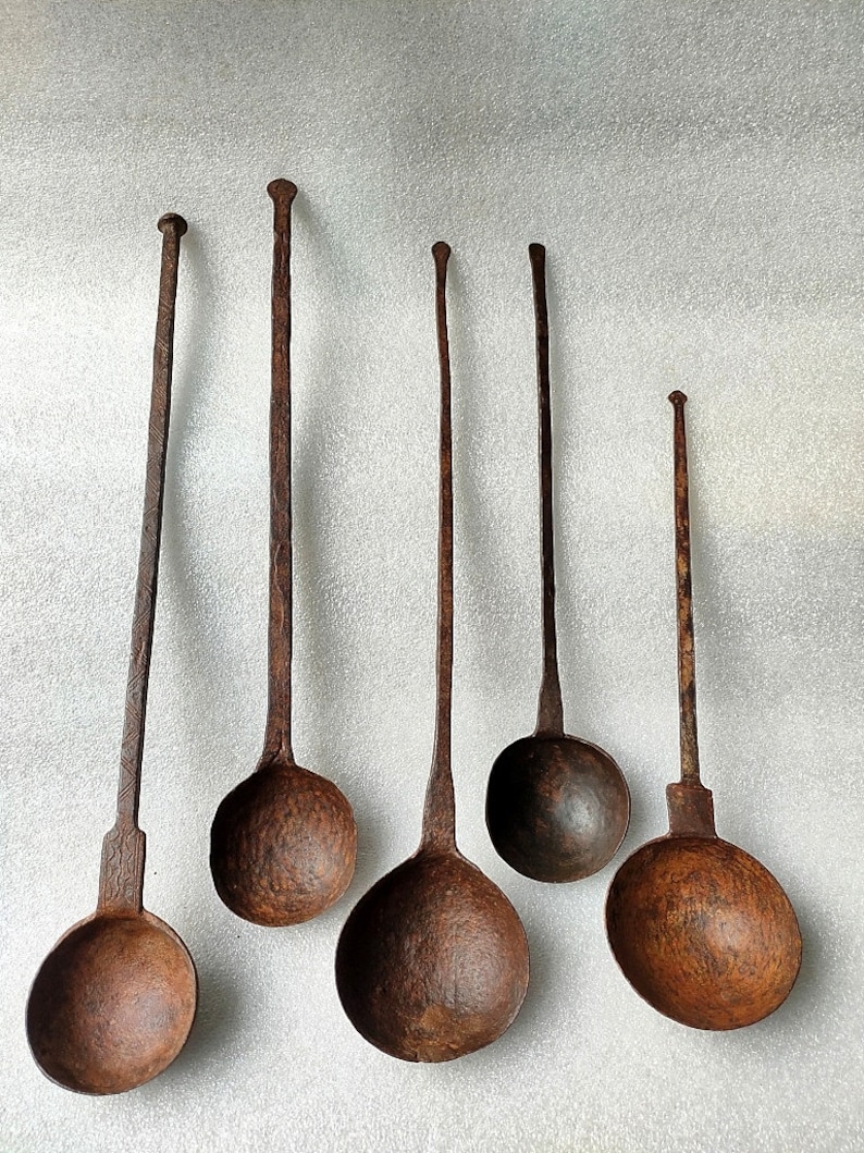 以下が含まれることがあります： 長い柄のついたアンティークの金属製のレードルが6つあり、サイズは様々です。レードルはさび付いており、茶色の緑青が付いています。