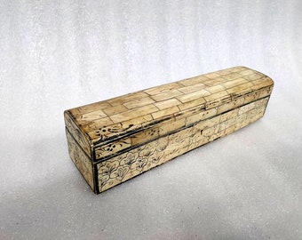 May include: A long, rectangular box with a hinged lid, featuring an off-white, cream-coloured surface composed of small, rectangular segments. The exterior is decorated with intricate, hand-drawn black floral patterns and line details.