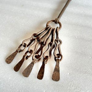 May include: A rusty metal chain with six blades attached to a long metal rod. The chain and blades are connected by a ring at the top of the rod.
