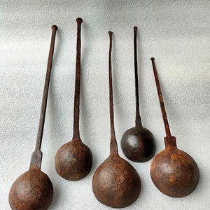 以下が含まれることがあります： 長い柄と丸いボウルを持つ、アンティークな鉄製のレードルが6本。レードルはさび付いており、濃い茶色の光沢があります。
