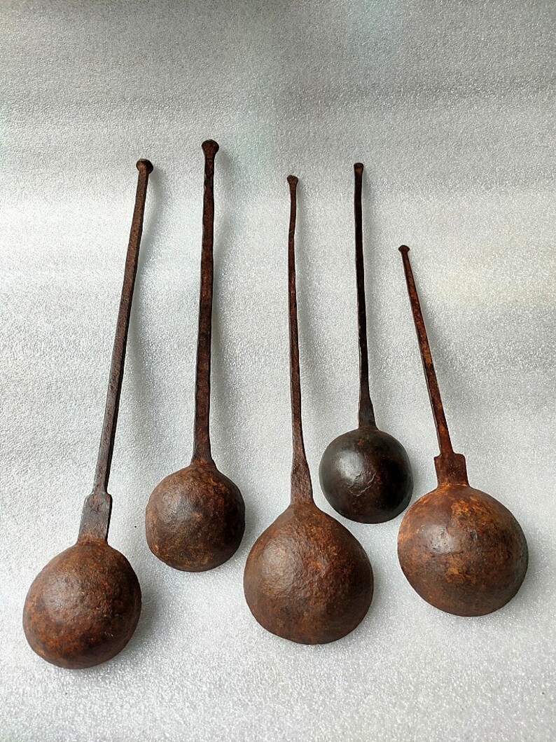 以下が含まれることがあります： 長い柄と丸いボウルを持つ、アンティークな鉄製のレードルが6本。レードルはさび付いており、濃い茶色の光沢があります。