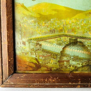Puede incluir: Una ilustraci&oacute;n vintage enmarcada de la Kaaba en La Meca, Arabia Saudita. La imagen est&aacute; en un marco de madera y presenta una representaci&oacute;n detallada del sitio sagrado, rodeado de edificios y una colina en el fondo.