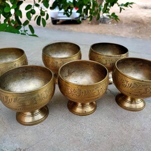 May include: Six antique brass bowls with a pedestal base and etched floral designs. The bowls have a rounded shape and a warm, golden color. These decorative bowls are ideal for serving or display.