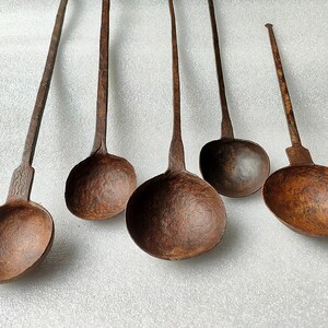 以下が含まれることがあります： さび付いた茶色のアンティークな鉄製のレードル5個セット。レードルは長いハンドルと丸いボウルが付いています。