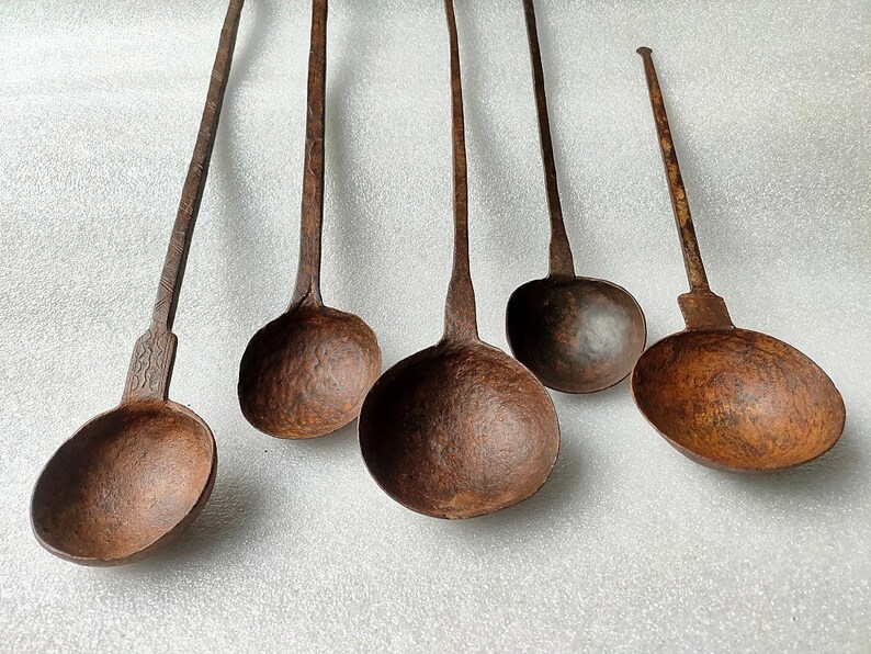 以下が含まれることがあります： さび付いた茶色のアンティークな鉄製のレードル5個セット。レードルは長いハンドルと丸いボウルが付いています。