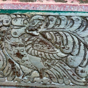 May include: A weathered wooden carving of a bird with intricate details. The carving is painted in shades of gray and brown, and the bird's wings are spread out.