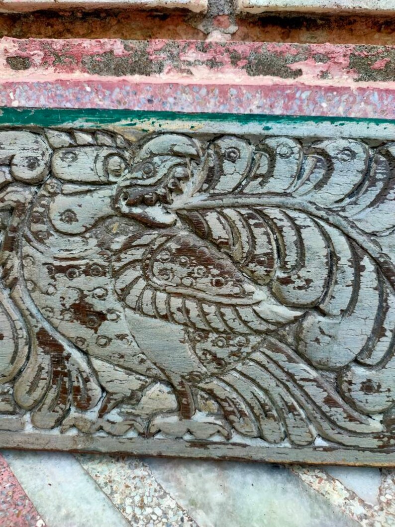 May include: A weathered wooden carving of a bird with intricate details. The carving is painted in shades of gray and brown, and the bird's wings are spread out.