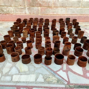 May include: A collection of weathered, cylindrical metal objects with a rusty brown patina. The objects are arranged on a patterned surface, varying in height and diameter. The overall impression is of aged, industrial components.