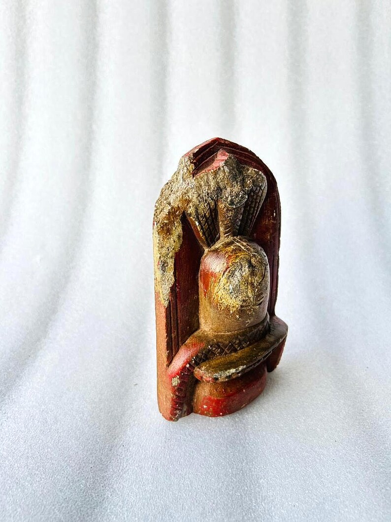 Puede incluir: Una peque&ntilde;a escultura de piedra tallada a mano de una deidad con un acabado de pintura roja y dorada. La escultura est&aacute; en posici&oacute;n de pie con una corona en la cabeza.