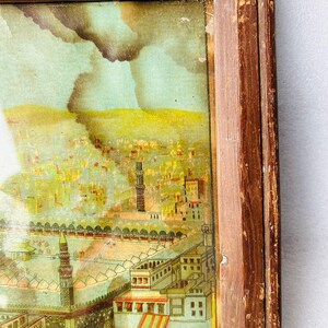 Puede incluir: Una ilustraci&oacute;n vintage enmarcada de una ciudad con una mezquita en primer plano. La ilustraci&oacute;n est&aacute; pintada en colores apagados con un cielo azul y edificios amarillos. El marco es de madera y tiene un acabado desgastado.